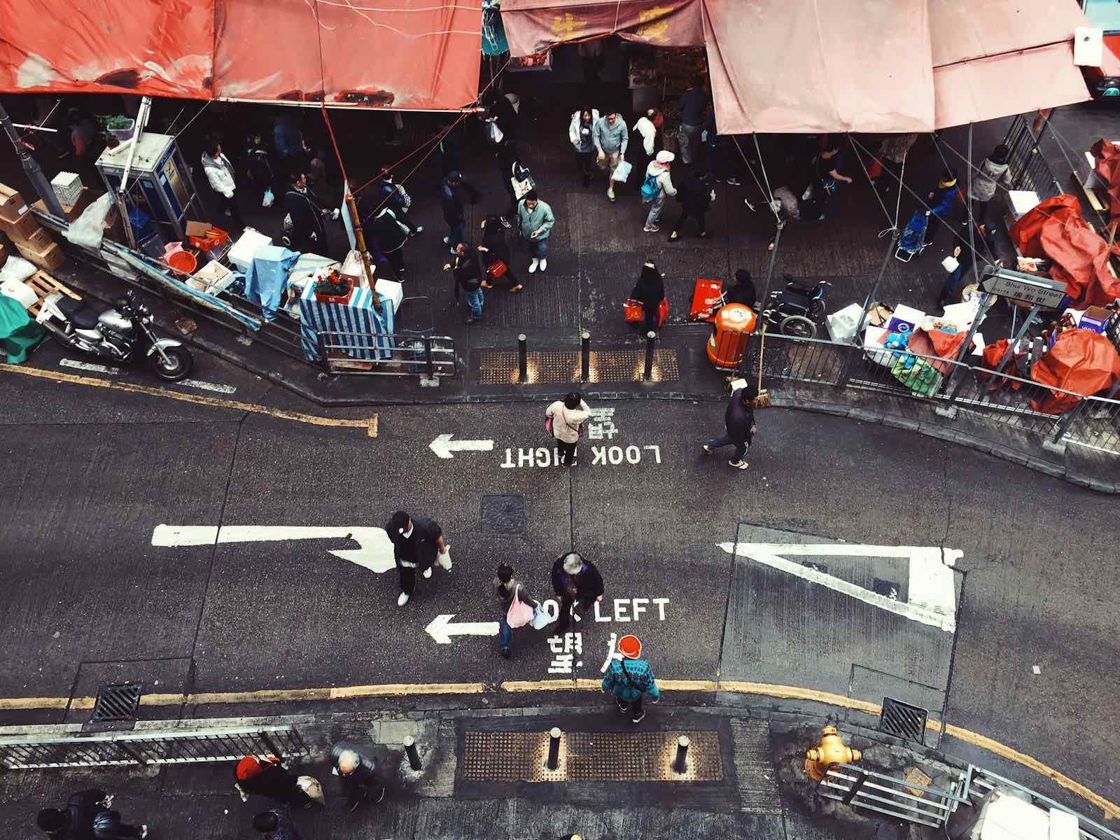 Crowded outdoor Asian market with vendors and shoppers under warm light.