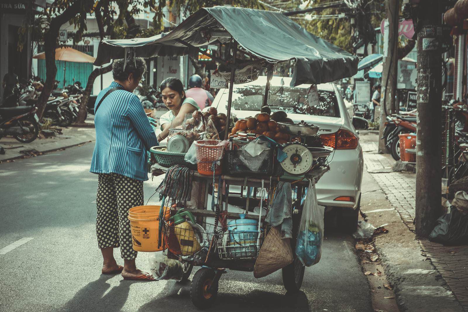 Two vendors selling fresh produce from a cart on a busy street in Vietnam.